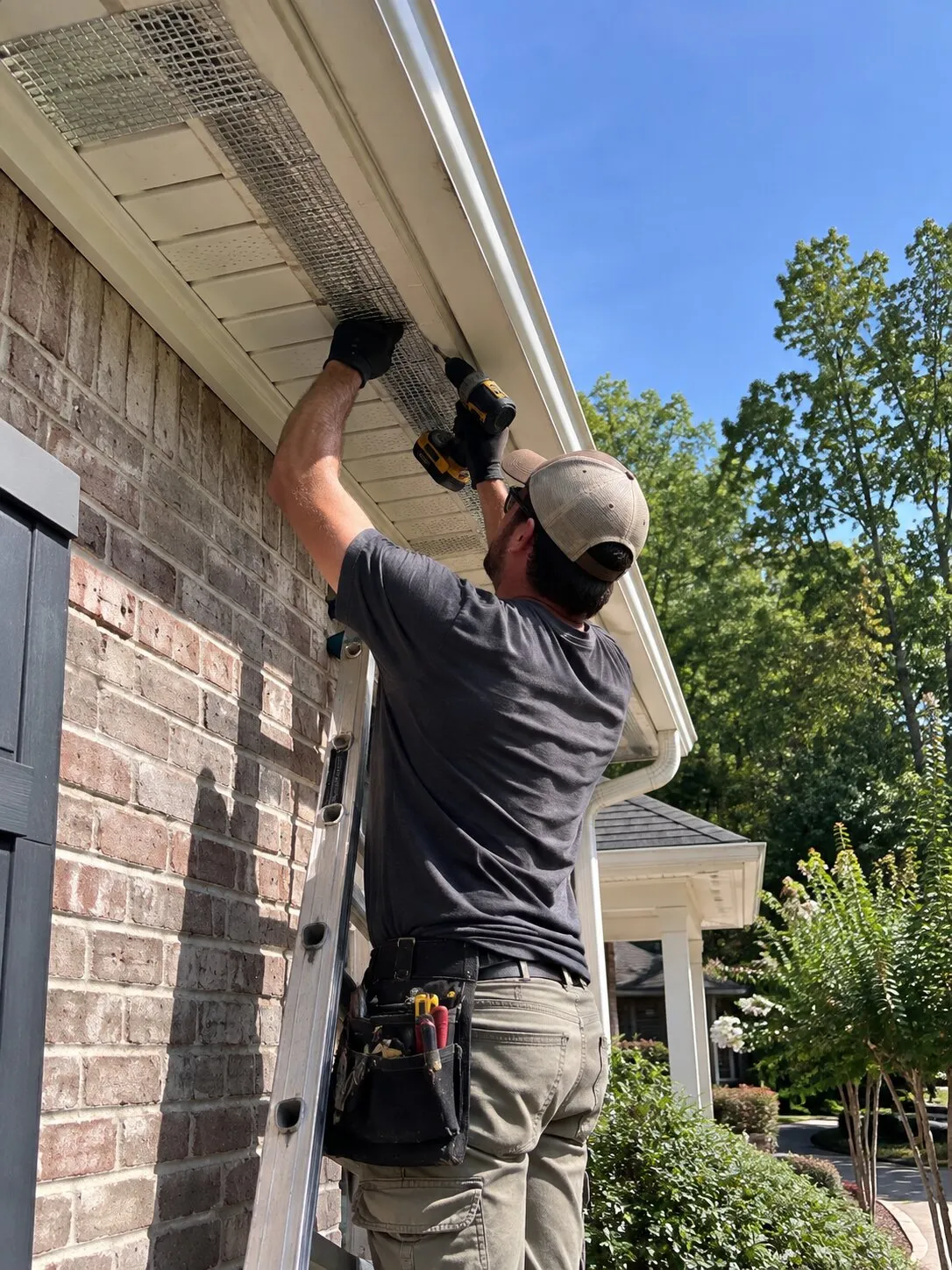 Technician working from a ladder to secure screening under a roof eave